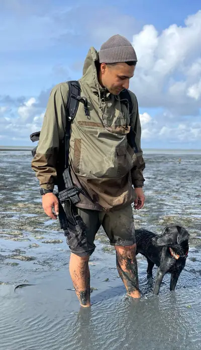 Sebastian Hamzian Hundetrainer steht im Watt mit schwarzer Labrador-Hündin